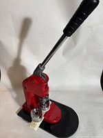 Front-side view showing the button maker's red metal body, black base, and lever handle.