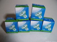 Six boxed CBconcept halogen GU10 120V bulbs shown stacked in a pyramid with green and blue packaging.