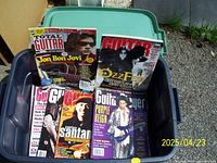 Photo showing guitar magazines in a plastic bin with covers featuring Jon Bon Jovi, Ozzy Osbourne, Carlos Santana, Prince, and others.