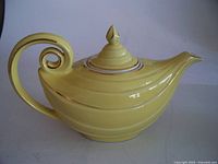 Full side view of yellow Hall teapot showing curled handle and pointed finial lid with gold trim.