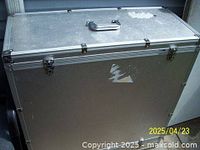Front view of large rectangular metal travel case showing handle and two metal latches. Surface has some scratches and wear patches.
