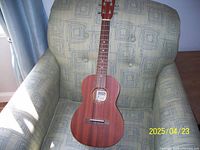 Full view of the Makai ukulele resting on a patterned armchair, showing wooden body and neck with four strings.