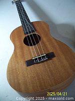 Front view of ukulele showing natural wood grain body with four-string bridge, missing one string.