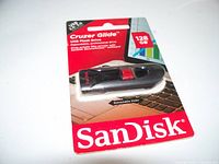 Photo of new SanDisk Cruzer Glide 128GB USB flash drive in sealed retail packaging showing front side with red and white packaging and product visible inside.