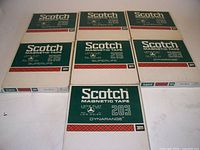 Seven 7-inch Scotch 3M magnetic tape reels in original packaging, mostly sealed cardboard sleeves with green and white design, five labeled 215 Superlife, two labeled 203 Dynarange.