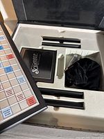 Scrabble Onyn Edition game board in storage box with tile racks, instruction booklet, and tile pouch in foam insert