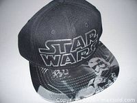 Black Star Wars baseball cap with white embroidered logo and printed Stormtrooper helmets on brim, displayed against a white background.