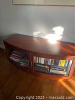 Wood stereo media cabinet with two glass-front doors placed against a white wall. Books inside the cabinet are visible through the glass doors. One door is detached and needs to be reattached as per the seller.