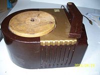 Vintage RCA record player with wooden body, felt turntable showing wear, gold control sliders, and a handle on the side.