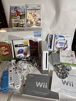 Overview of the Nintendo Wii system, games, and accessories including white console, power adapter, sensor bar, multiple Wii Remotes, game cases, and manuals.