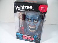 Front view of Yahtzee The Walking Dead Collector's Edition showing clear box with blue zombie head dice cup and red dice visible inside.