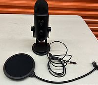 Black Blue Yeti USB podcast microphone with stand, pop filter, and USB cable visible on white surface with orange background.