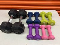 Photo showing two large rubber hex dumbbells with chrome handles and four pairs of smaller colorful neoprene coated dumbbells in blue, yellow, purple, and pink.