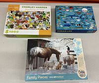 Photo showing three jigsaw puzzle boxes: Charley Harper 1000-piece puzzle, Ocean Life puzzle, and Cobble Hill 'Family Pieces' 350-piece puzzle.