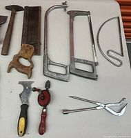Close-up of smaller hand tools including coping saw, hand drill, scraper, punch, scissors, and a caliper.