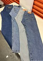 Four pairs of jeans folded and laid side by side showing back pocket and waistband details on table.