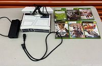 Shows limited edition R2-D2 style Xbox 360 console with Kinect sensor, power adapter, and six games laid out on table.