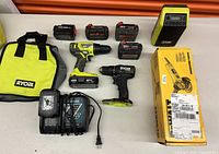 Overall view containing Ryobi tools, batteries, speaker, Makita charger, DeWalt grinder in box, and tool bag