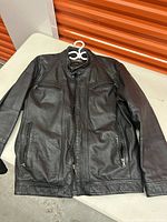 Full view of men's black leather jacket laid flat showing front zipper and pockets