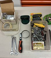 Photo showing multiple hand tools including wrenches, ratchet wrench, screws, hose clamp and other hardware items on table