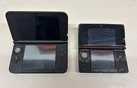 Front view of open Nintendo 3DS XL Luigi Edition and standard 3DS showing dual screens and control buttons.