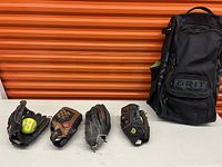 Photo showing all four mitts arranged in a row along with one yellow softball in the first mitt and the GRIT branded sports bag.
