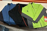 Three Spyder men's motorcycle jumpers in blue, black, and lime green laid out on a surface.