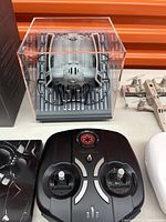 Photo showing a Propel Star Wars TIE Fighter drone inside a clear display case and a black Propel controller with joysticks and Star Wars Imperial logo.