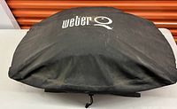 Black Weber Q grill cover with drawstring shown flat on table