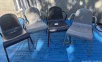 Four metal chairs, two grey and two black, arranged side by side on a blue painted surface outdoors.