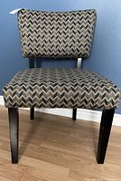 Front view of a fabric accent chair with a chevron pattern in brown and beige tones, wooden legs, and cushioned seat and backrest.