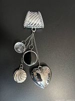Photo showing silver-tone sweater necklace clip with three hanging decorative charms in black and silver tones, against black background.