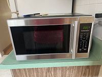 Front view of the microwave showing the stainless steel and black external casing, digital display active at 0:00, keypad on the right side, and handle on the right door.