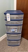 Front view of blue storage tower with 5 transparent drawers and blue frame, with a label and lot tag attached.