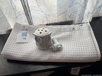 Folded white textured cloth shower curtain with metal grommets and grey owl-shaped plugin air freshener on top.