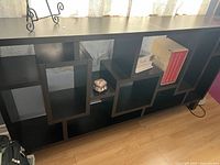 Front view of black geometric bookcase shelf with decorative items inside compartments such as books and small decor pieces