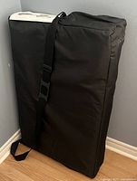 Folded massage table inside black carry bag with adjustable shoulder strap, showing compact storage form.