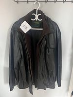 Black Danier men’s leather jacket hanging on a white plastic hanger, shows the front and sleeves with visible zipper and pockets.