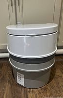 Full view of the portable chemical toilet showing white upper section with seat and lid and grey base tank.