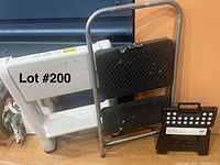 Overview photo showing the white plastic two-step ladder, black metal frame two-step ladder, and small black one-step stool grouped together on a wooden floor.