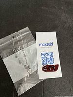 Swarovski magic necklace in small clear plastic bag alongside MaxSold identification card.