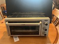 Front view of silver and black T-fal toaster convection oven with glass door, handle, and three control knobs.
