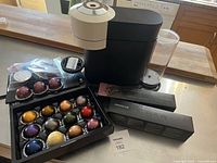 Box of assorted Nespresso coffee capsules in various colors including purple, gold, red, copper, green, silver, blue, and bronze.