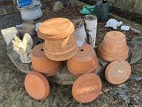 Photo of clay terra cotta planters stacked outdoors with matching saucers arranged on the ground.