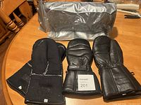 Photo showing the leather gloves and fabric inserts alongside a gray carrying case on a wooden table, displaying size labels and lot tag.