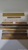 Top view of 11 vintage advertising rulers showing a variety of wood and plastic materials, lengths, and printed company names.