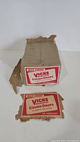 Front view of original cardboard box with clear Wild Cherry Vicks Medicated Cough Drops labeling and condition showing wear and tear.