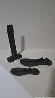 Two cast iron shoe molds lying flat on a white surface with one vertical cast iron stand behind them
