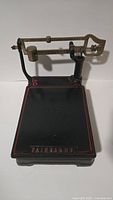 Front view of the antique scale showing the cast iron base with red painted border lines and the brass balance bar arm above.