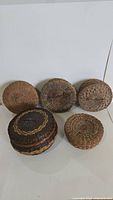 Group photo showing five round woven sewing baskets, four in natural reed shades and one darker with braided accent on lid